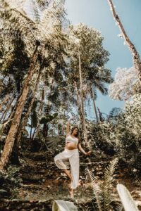 Woman Standing between Palm Trees on One Leg with an Arm Raised